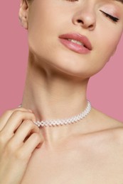 Young woman wearing elegant pearl necklace on pink background, closeup