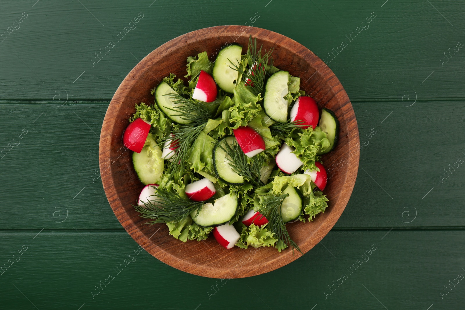 Photo of Delicious salad with radish, lettuce, dill and cucumber on green wooden table, top view