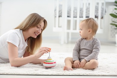 Children toys. Happy mother and her little son playing with spinning top on rug at home