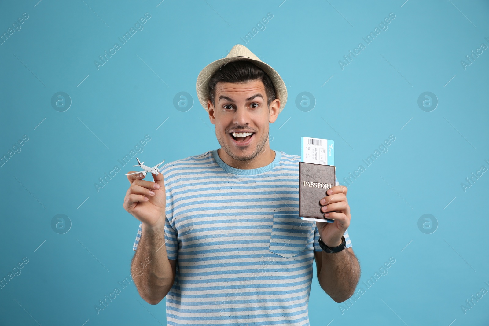 Photo of Excited male tourist holding passport with ticket and toy airplane on turquoise background