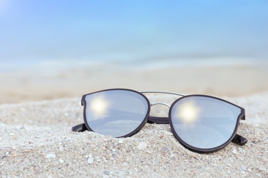 Stylish sunglasses on sandy beach near sea