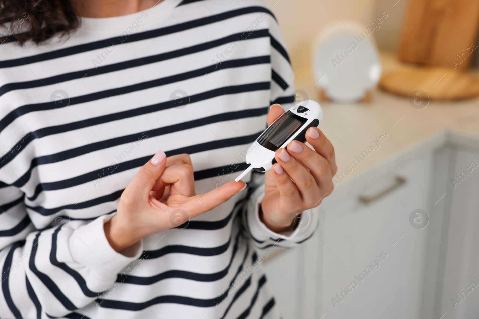 Photo of Diabetes. Woman checking blood sugar level with glucometer in kitchen, closeup. Space for text