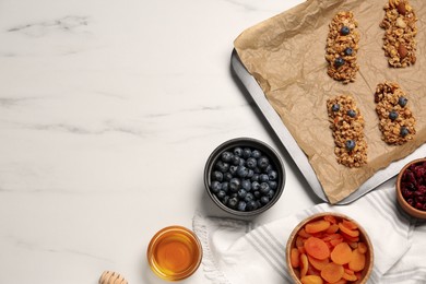 Making granola bars. Baking tray and ingredients on white marble table, flat lay. Space for text