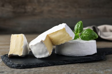 Photo of Tasty cut and whole brie cheeses with basil on wooden table