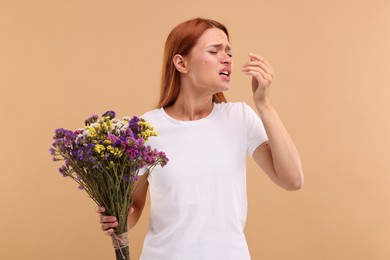 Photo of Suffering from allergy. Young woman with flowers sneezing on beige background