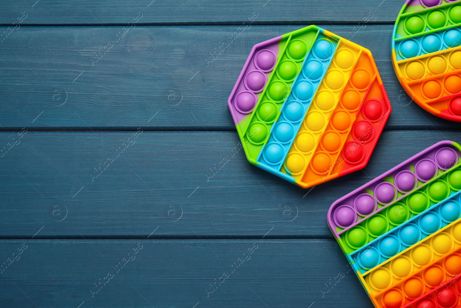 Photo of Rainbow pop it fidget toys on blue wooden table, flat lay. Space for text