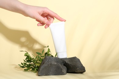 Woman with tube of cream, branches and stones on light yellow background, closeup