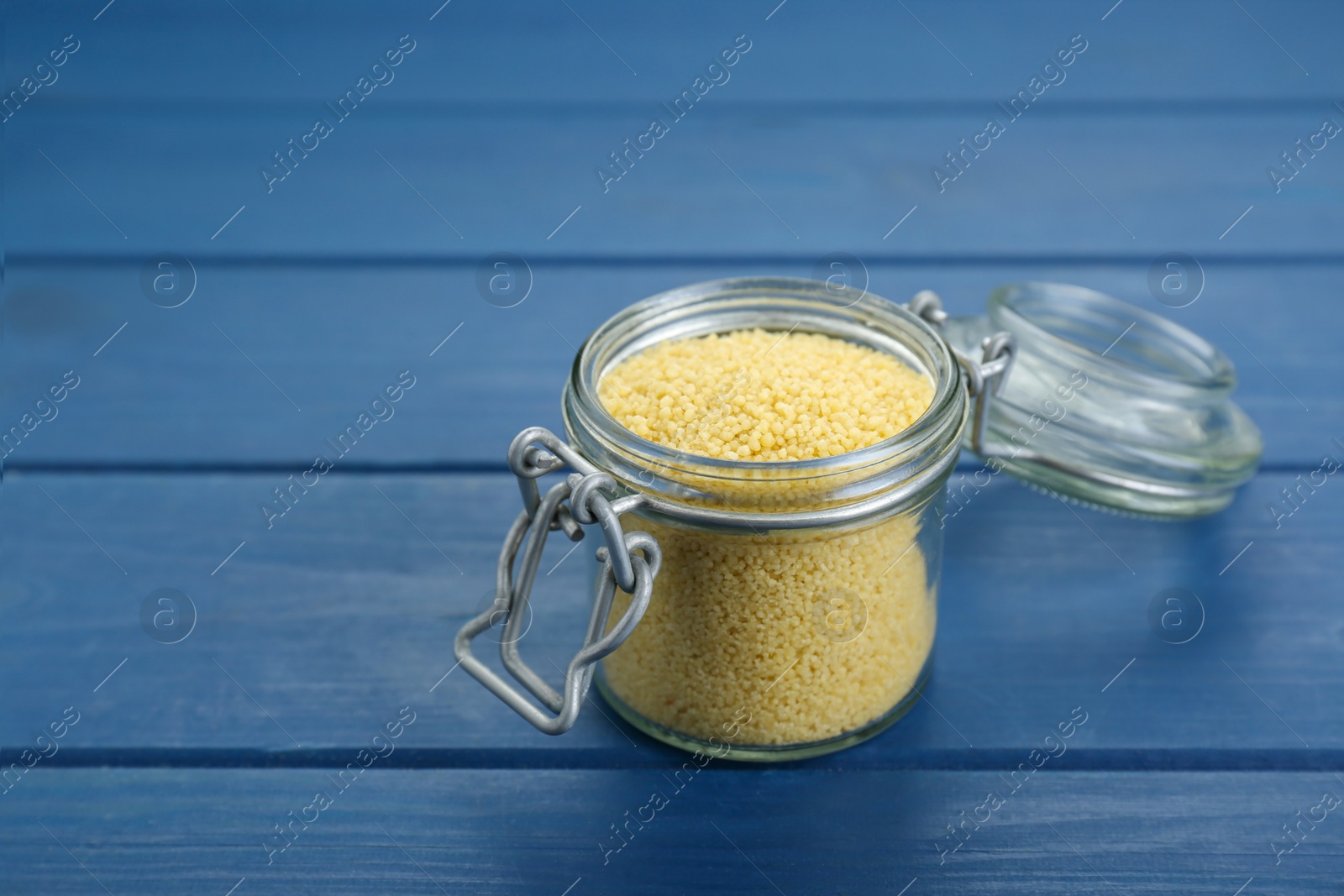 Photo of Glass jar of raw couscous on blue wooden table, closeup. Space for text