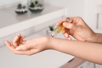 Woman applying essential oil on wrist indoors, closeup