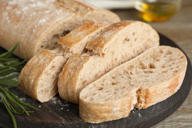 Cut delicious ciabatta with rosemary on table, closeup