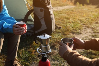 Photo of Young couple drinking coffee near camping tents outdoors, closeup