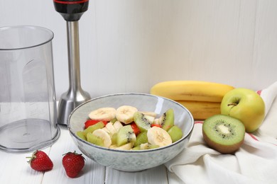Photo of Hand blender kit, fresh fruits and strawberries in bowl on white wooden table