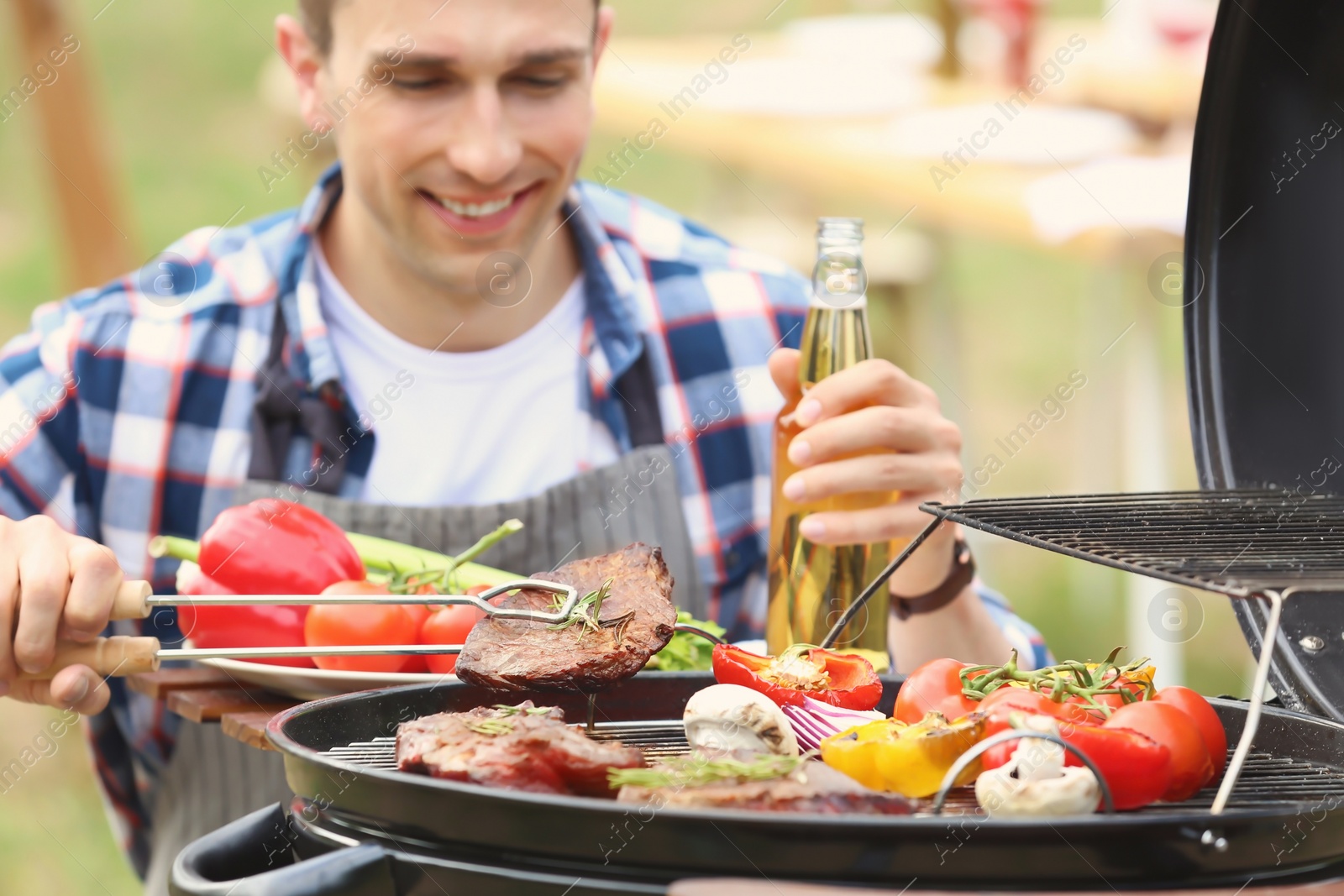 Photo of Young man cooking meat and vegetables on barbecue grill outdoors