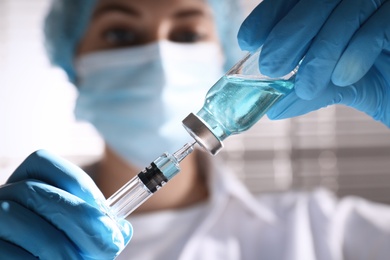 Photo of Woman filling syringe with vaccine from vial on blurred background, closeup