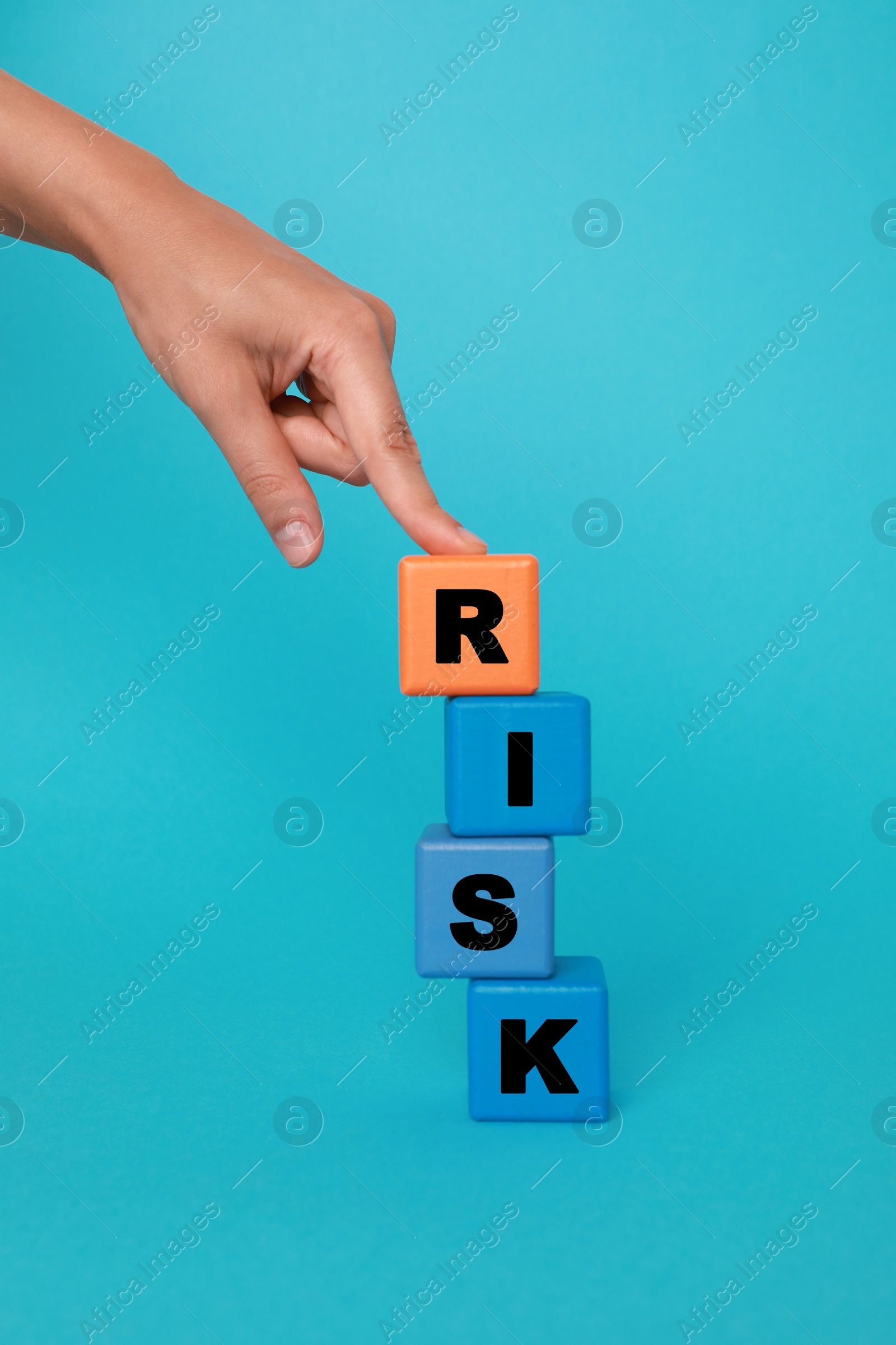 Photo of Woman making word Risk with colorful cubes on turquoise background, closeup