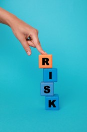 Photo of Woman making word Risk with colorful cubes on turquoise background, closeup