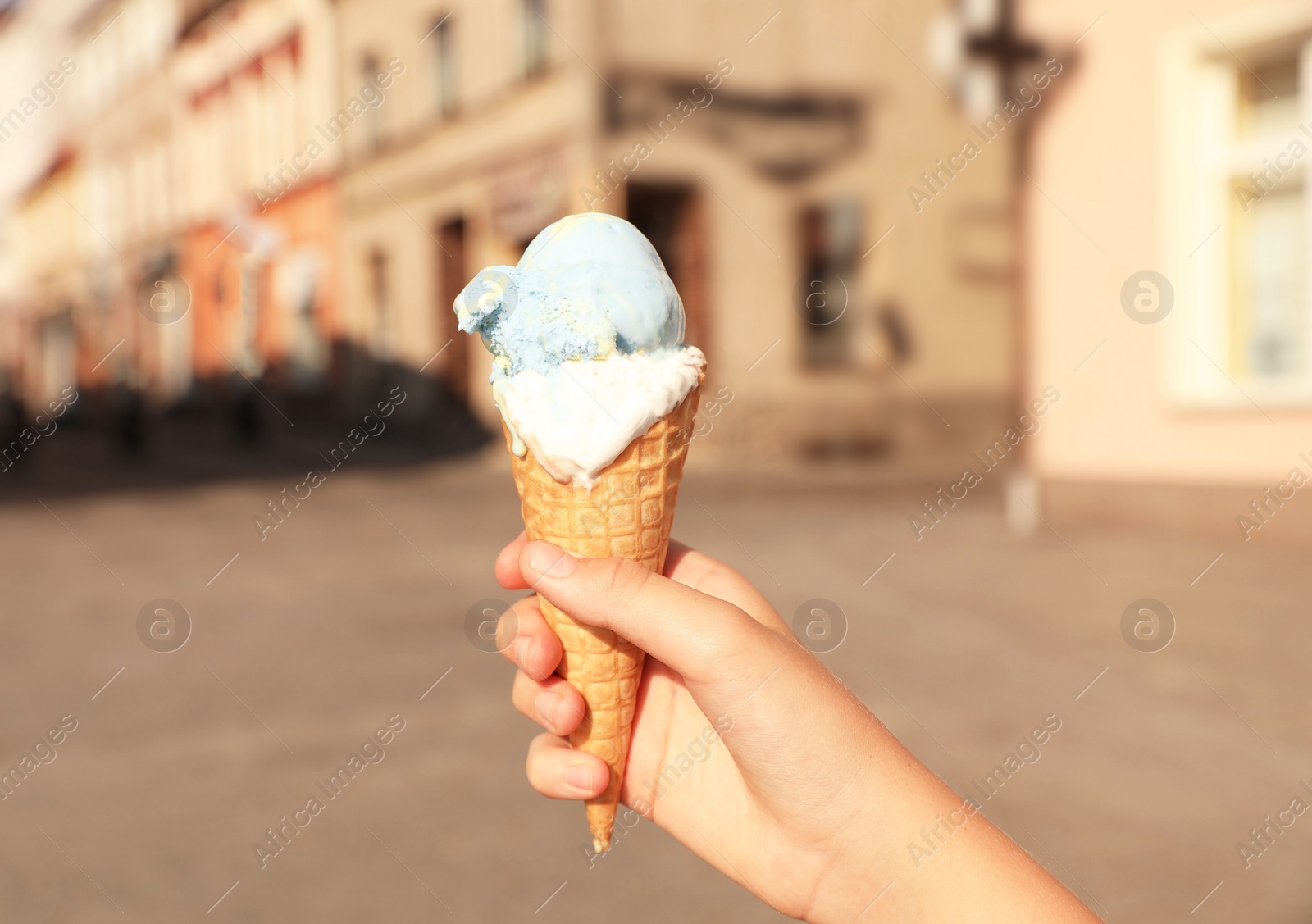 Photo of Woman holding delicious ice cream in wafer cone in city, closeup