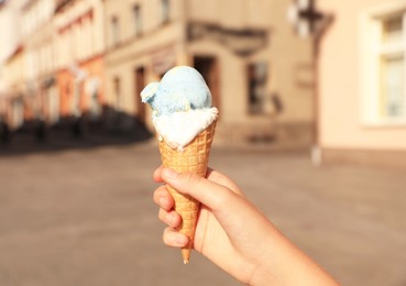 Photo of Woman holding delicious ice cream in wafer cone in city, closeup