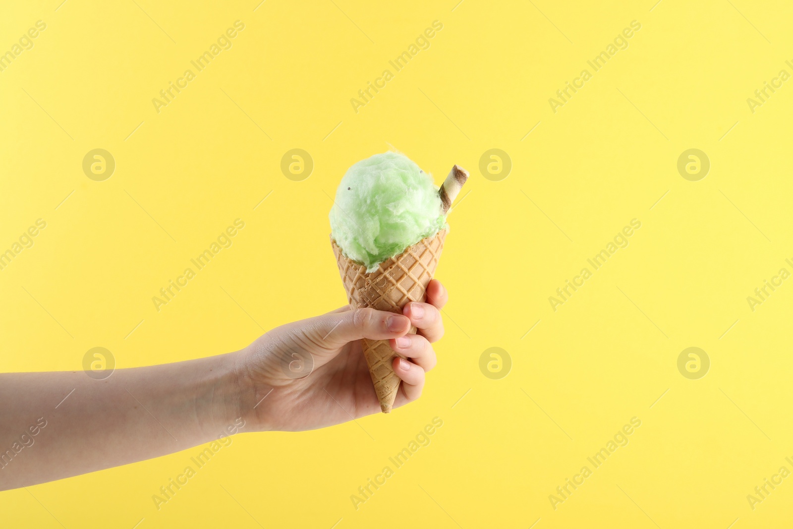 Photo of Woman holding waffle cone with cotton candy on yellow background, closeup