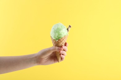 Photo of Woman holding waffle cone with cotton candy on yellow background, closeup