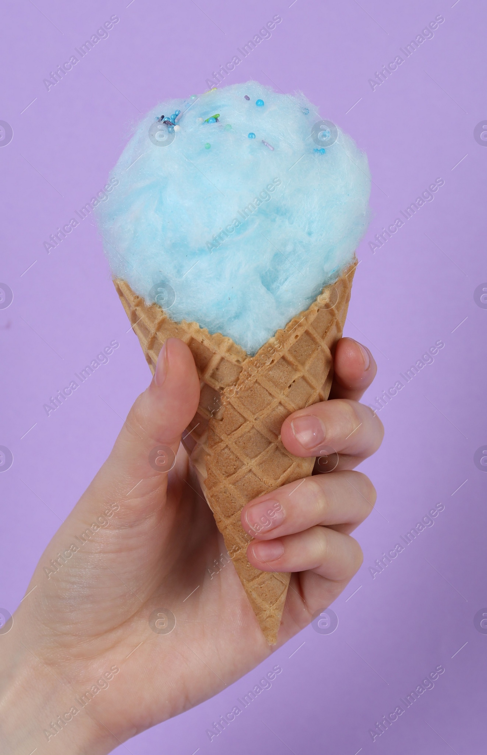 Photo of Woman holding waffle cone with cotton candy on violet background, closeup