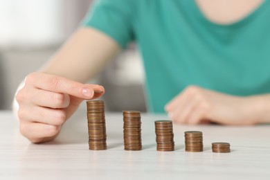 Photo of Financial savings. Woman stacking coins at white wooden table indoors, closeup