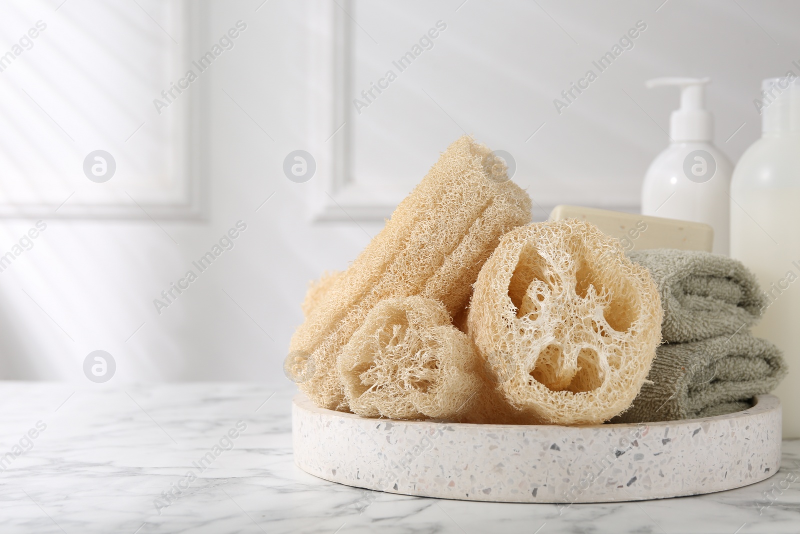 Photo of Loofah sponges, towels and soap on white marble table, space for text