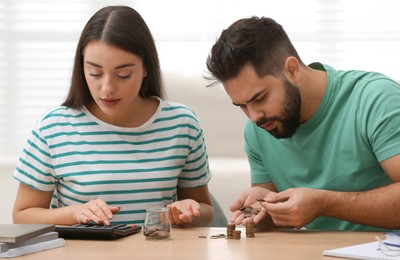 Young couple counting money at wooden table indoors