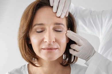 Photo of Doctor examining mature woman face before cosmetic surgery on white background
