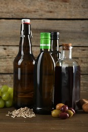 Photo of Vegetable fats. Different cooking oils in glass bottles and ingredients on wooden table