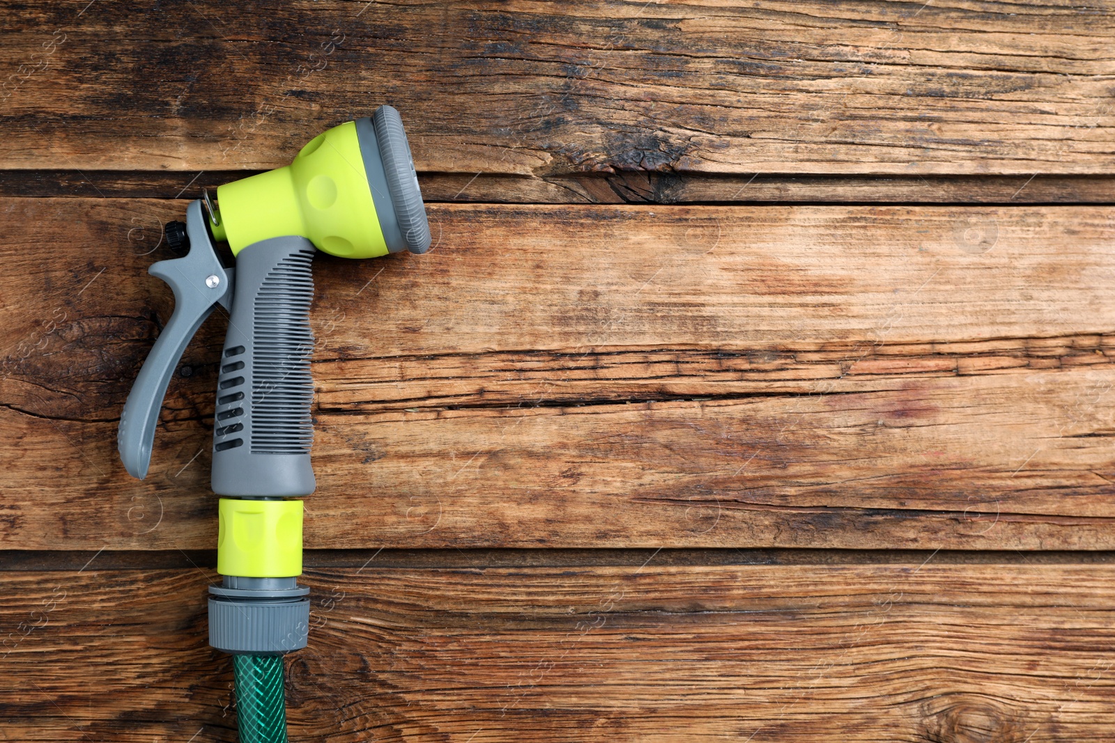 Photo of Green garden hose with spray gun on wooden table, top view