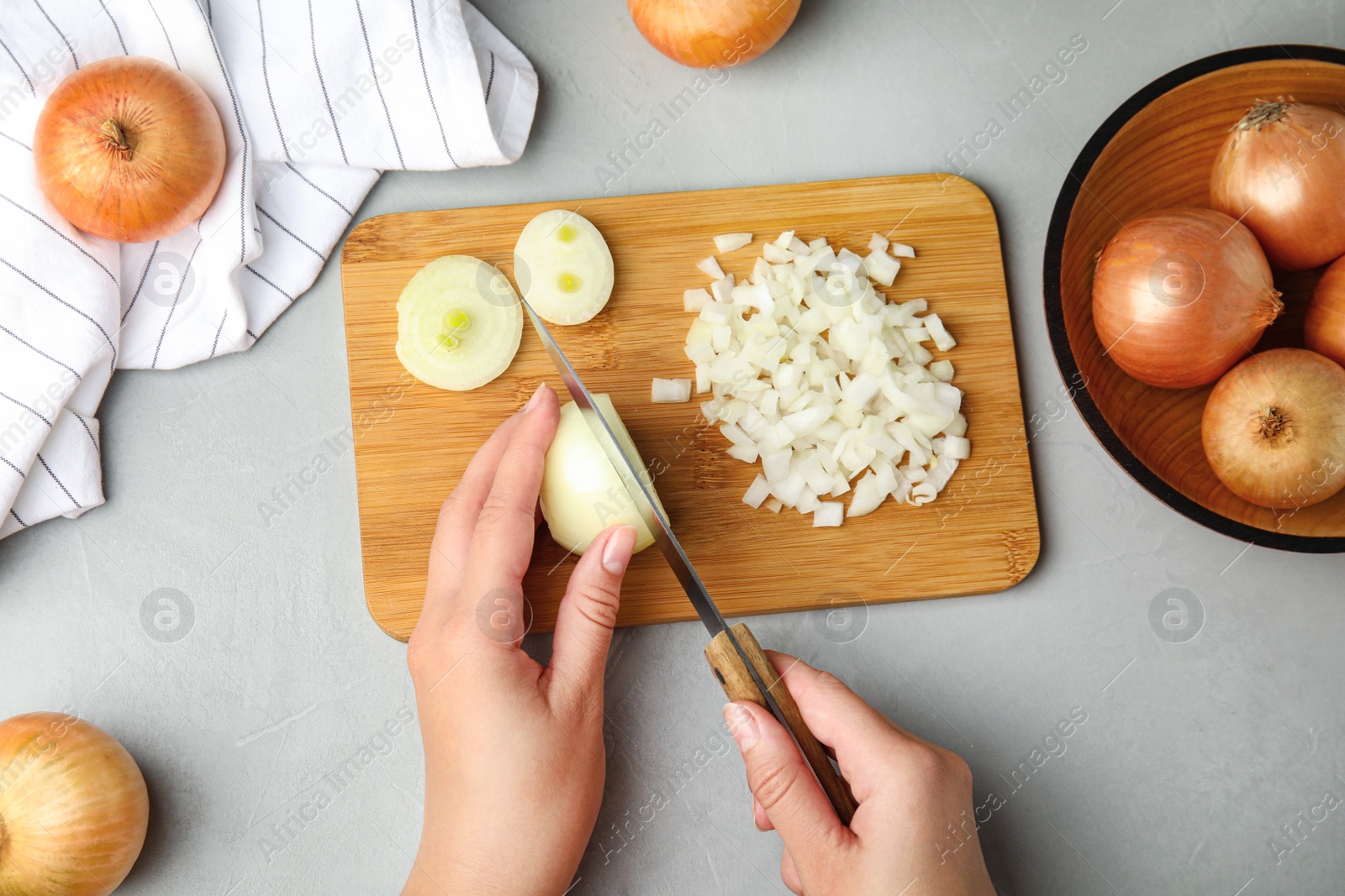 Photo of Woman cutting ripe onion on wooden board at grey table, top view