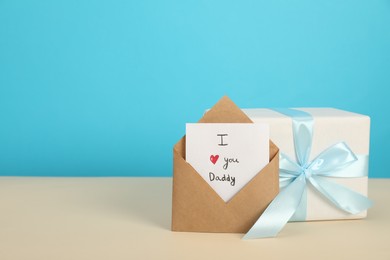 Photo of Happy Father's Day. Card with phrase I Love You, Daddy in envelope and gift box on beige table, closeup. Space for text