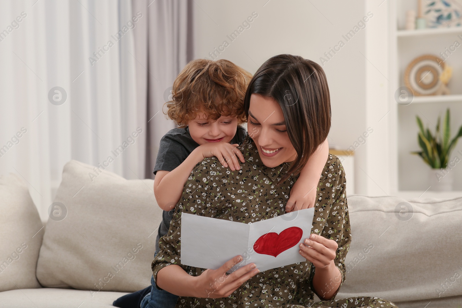 Photo of Little son congratulating his mom with Mother`s day at home. Woman holding handmade greeting card