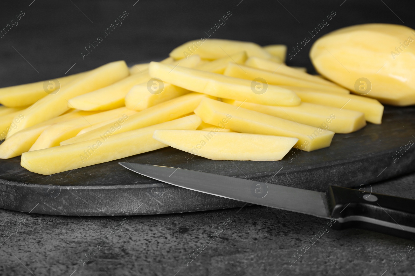 Photo of Whole and cut raw potatoes with knife on grey table, closeup. Cooking delicious French fries