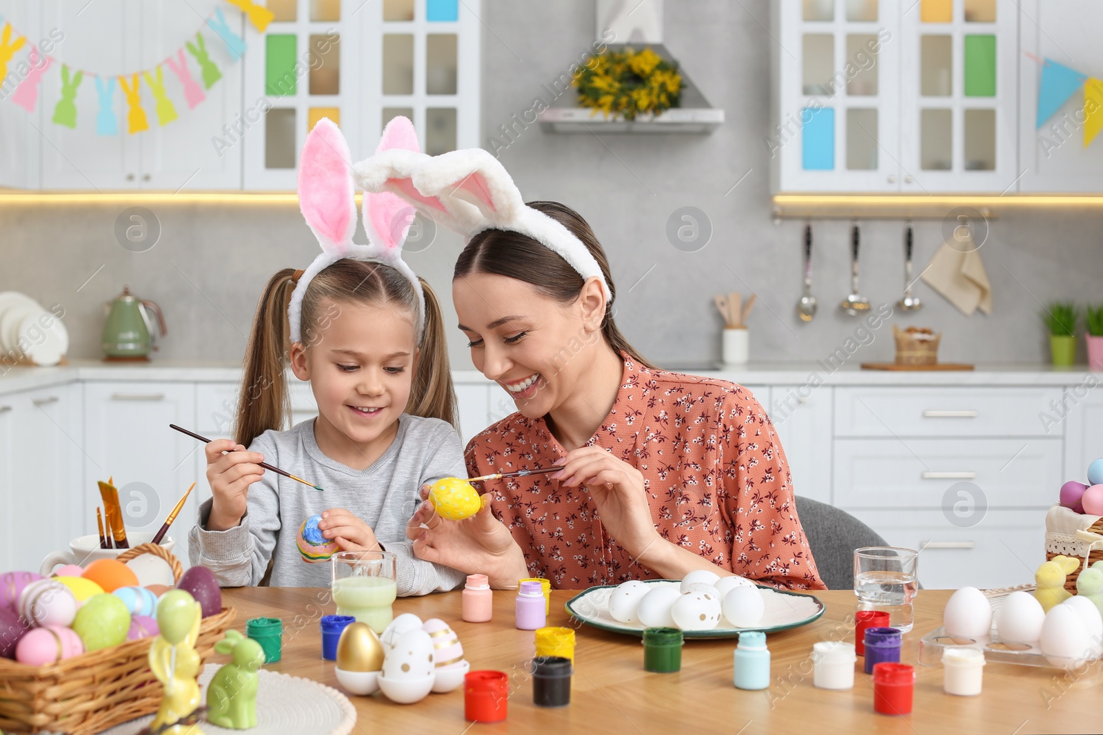 Photo of Mother and her cute daughter painting Easter eggs at table in kitchen