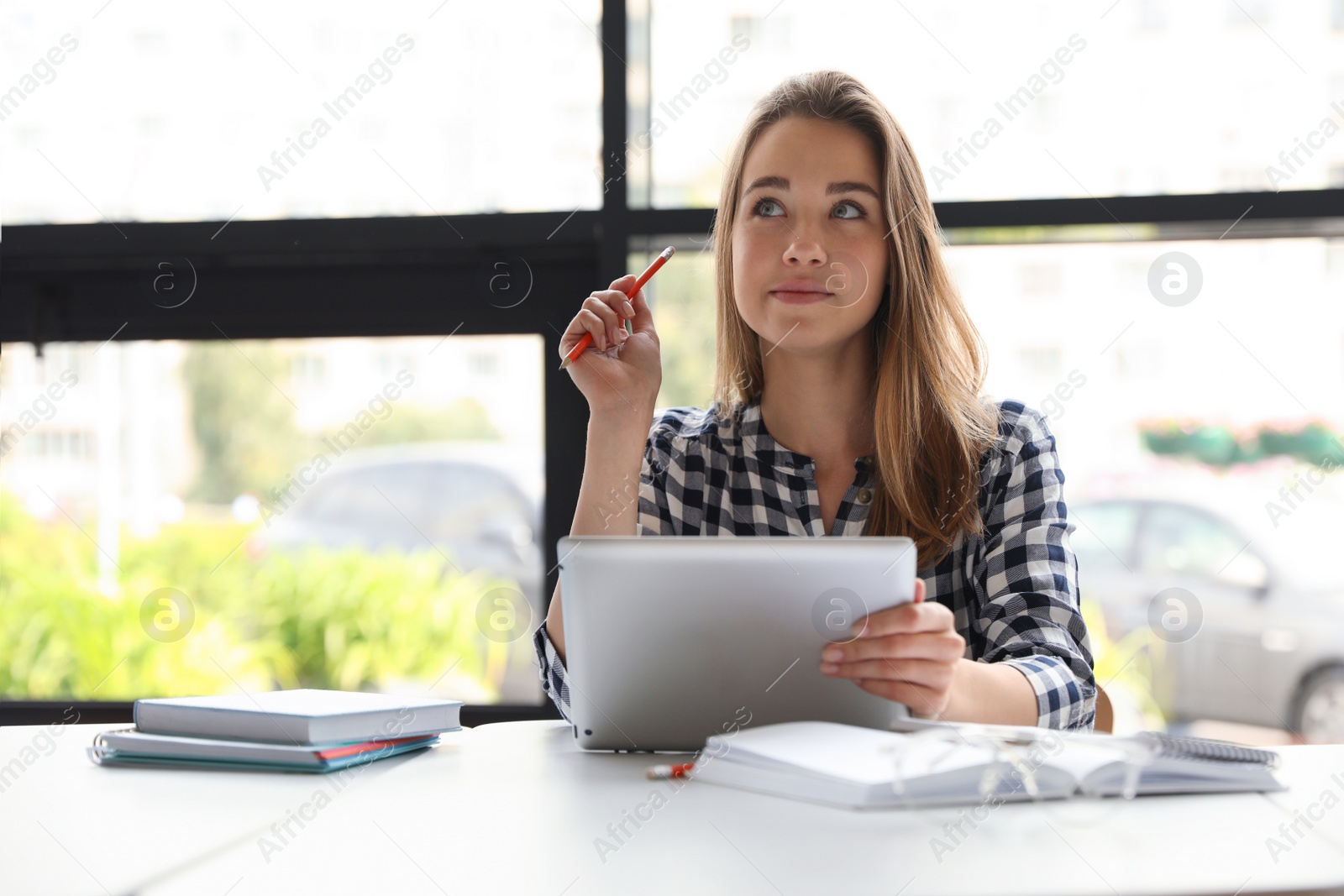 Photo of Pensive young woman studying with tablet at table in library