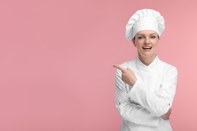 Photo of Happy chef in uniform pointing at something on pink background, space for text