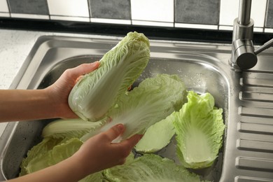 Photo of Woman washing fresh Chinese cabbages in sink, closeup