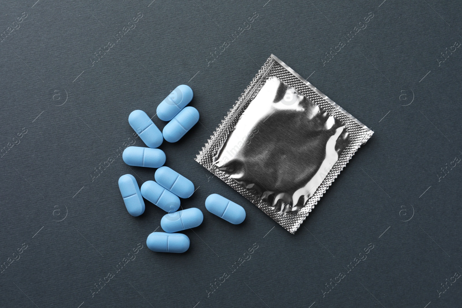 Photo of Pills and condom on dark gray background, flat lay. Potency problem
