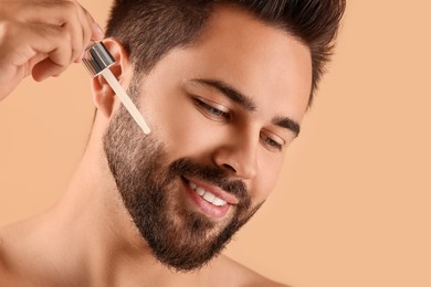 Photo of Handsome man applying cosmetic serum onto face on beige background, closeup