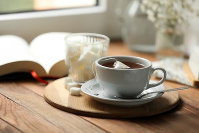Photo of Tray with cup of freshly brewed tea and sugar cubes on wooden table, space for text