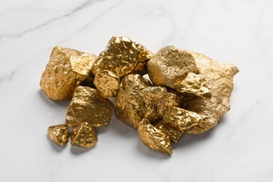 Pile of shiny gold nuggets on white marble table