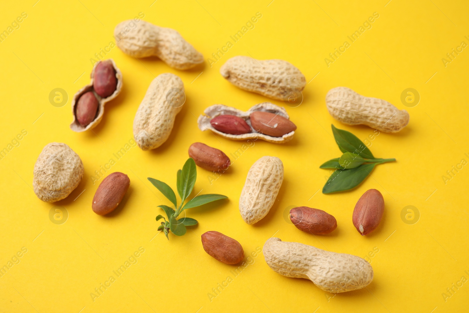 Photo of Fresh peanuts and leaves on yellow table, closeup