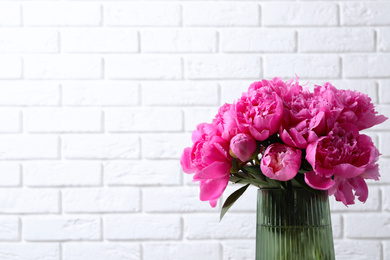 Photo of Bouquet of beautiful peonies in vase near white brick wall. Space for text