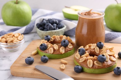 Photo of Slices of fresh apple with peanut butter, blueberries and nuts on white marble table, closeup