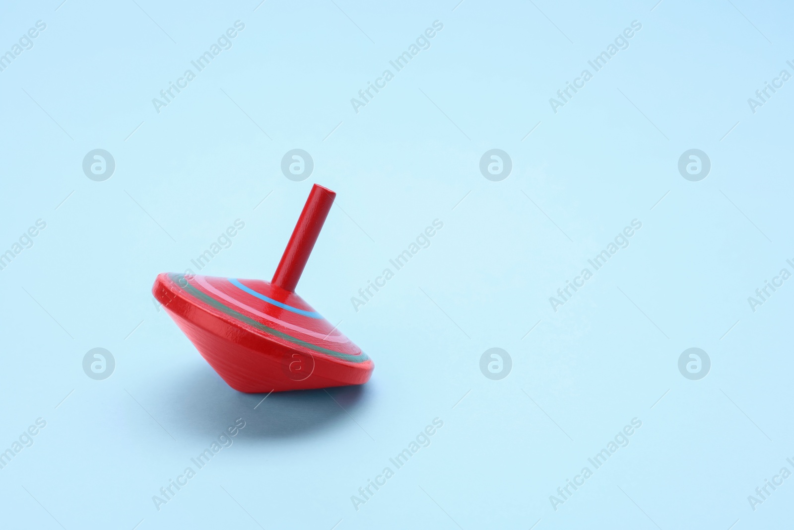 Photo of One bright spinning top on light blue background, space for text. Toy whirligig