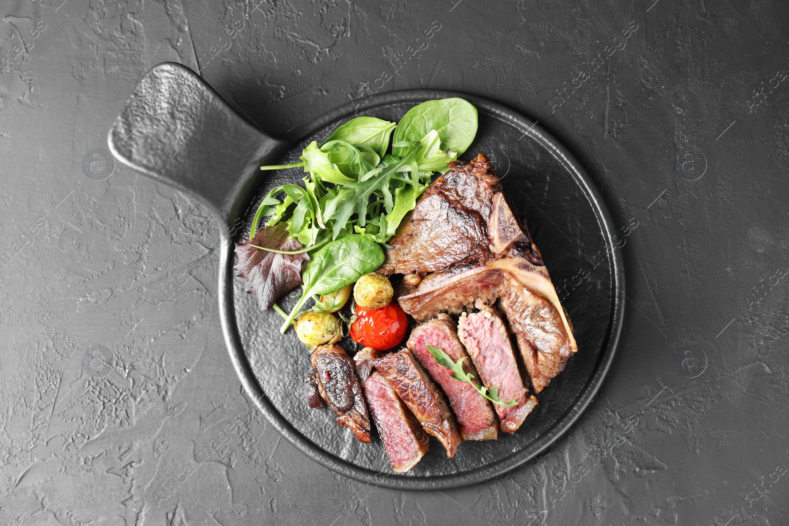 Photo of Delicious grilled beef meat, vegetables and greens on black table, top view