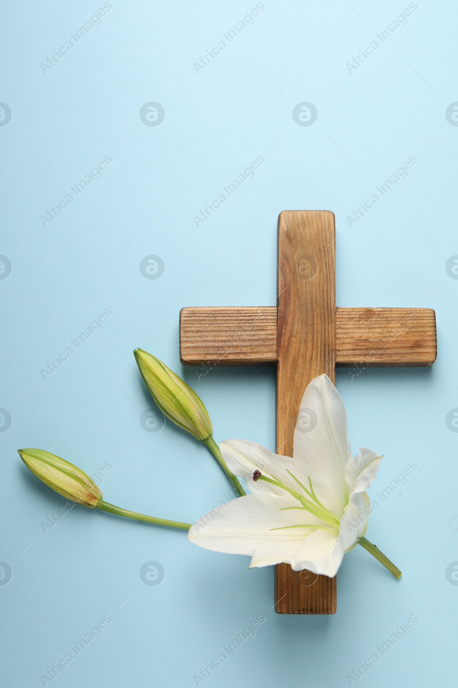 Photo of Wooden cross and lily flowers on light blue background, top view. Easter attributes