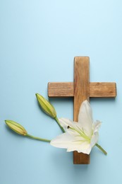 Photo of Wooden cross and lily flowers on light blue background, top view. Easter attributes